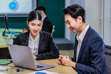 Millennial Asian professional successful male businessman manager mentor helping coaching advising new female businesswoman employee staff in formal business suit sitting working with laptop computer