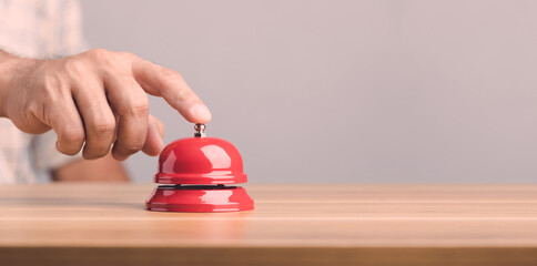Hand ringing the red call bell or service bell ring on the brown wooden desk with grey wall background. For hotel or restaurant advertising concept