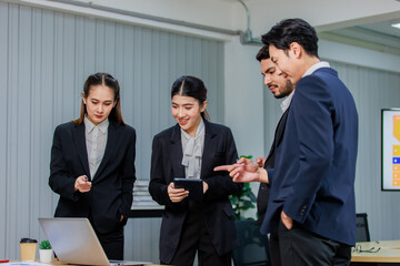 Millennial Asian Indian professional male businessmen female businesswomen employee staff colleagues in formal business suit standing discussing brainstorming working together with laptop computer