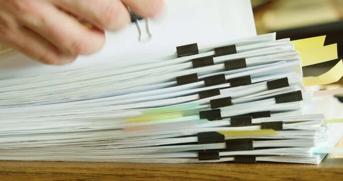 Fingers fingering a large stack of paper documents.