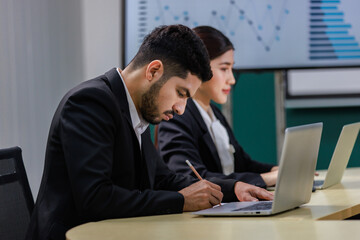 Millennial Asian professional female businesswoman audience in formal business suit sitting looking at laptop notebook computer screen in company office meeting room with Indian male businessman
