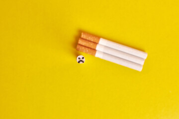 Cigarettes on a yellow background with a cigarette with sad emotions. The concept of the bad habit of smoking.