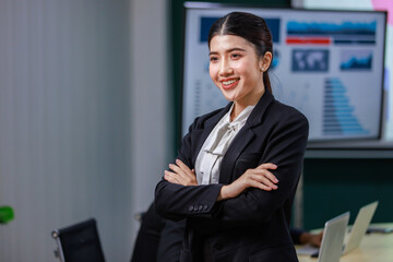 Fototapeta premium Millennial Asian professional successful female businesswoman entrepreneur ceo management in formal business suit standing smiling crossed arms posing taking portrait in company office meeting room