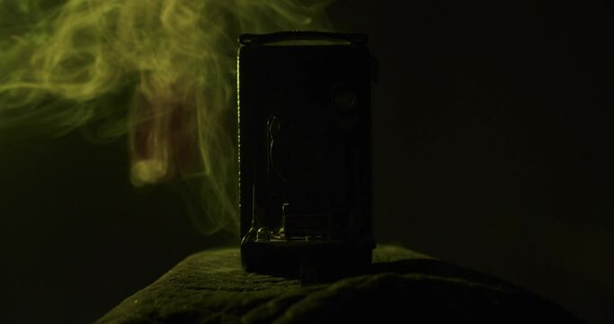 Yellow smoke behind a very old vintage folding camera from 1910 in a dark room