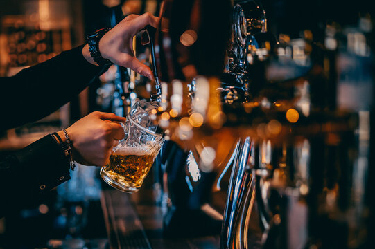 man bartender hand at beer tap pouring a draught beer in glass serving in a restaurant or pub