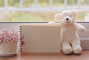 Handmade notebooks made from mulberry paper. placed horizontally by the white window Beside a white cute teddy bear with a small pot of tea ribbon plant, green nature background.