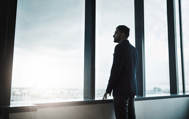 On a whole new level. Shot of a young businessman looking thoughtfully out of an office window.