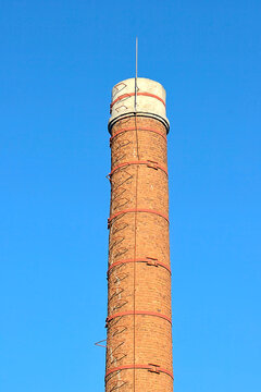 A tall brick chimney with a lightning rod against a blue sky
