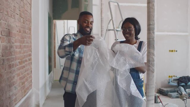 African-American Couple Have Fun With Bubble Wrap Renovating Apartment. Realtime