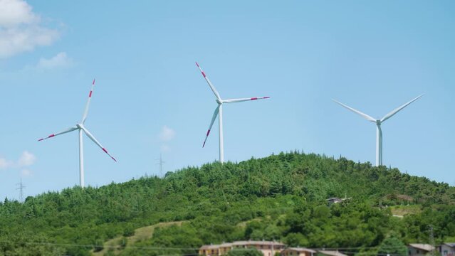 Three wind turbines rotate above green hills