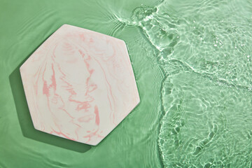 Hexagon podium on transparent clear green water texture with splashes and waves in sunlight. View...