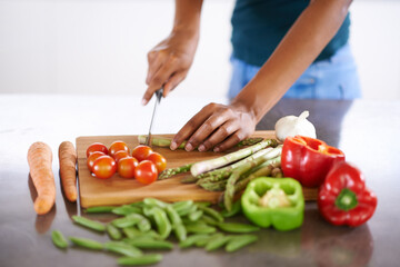 Preparing a healthy and wholesome meal. Cropped closeup shot of a woman cutting up vegetables on a cutting board. - Powered by Adobe