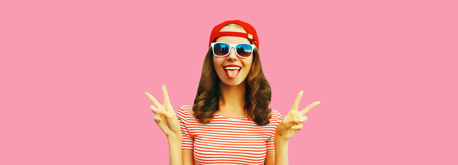 Portrait of happy cheerful smiling young woman having fun showing her tongue wearing red baseball...
