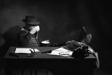Black and white, noir, vintage photography. Man, professional detective in hat sitting at table and...