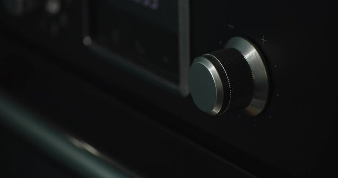 Person turning up temperature knob of black oven in home kitchen, close up