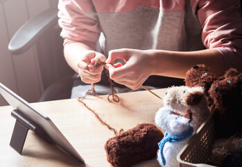 Obraz premium A young woman sits at a table and knits with her knitting needles, using a clipboard to learn.