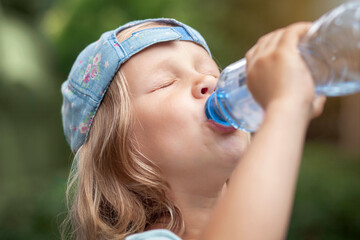 Drinking Water from Bottle. Thirsty Child Little Girl Baby Drink Water on Green Nature Background Outside.