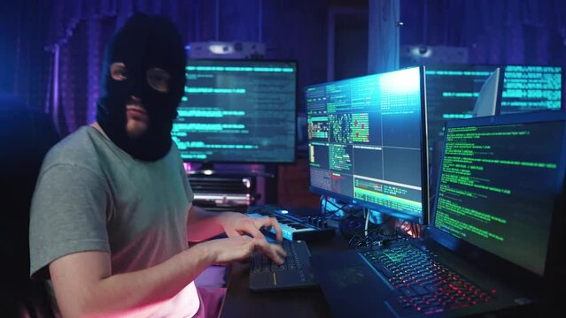 Hacker Coding and Listening Music on Programming Computer at Table. Male Anonymous Individual Looking at Notebook and Hacking PC in Neon Color Light. IT Cybercrime of Thief Mask Hacks Virtual Database