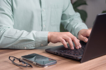 Closeup image of a young man working and typing on laptop computer keyboard on wooden table in the cafe.