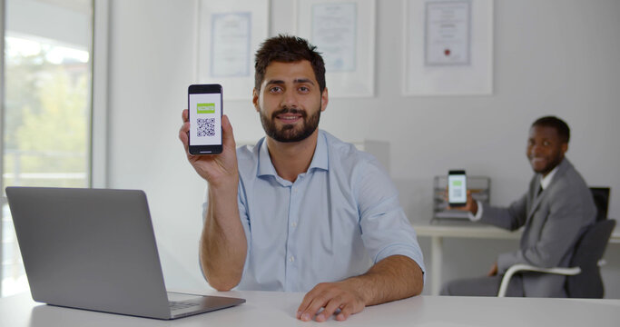 Diverse office workers smiling at camera showing smartphone with vaccinated qr-code - Powered by Adobe