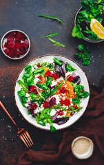 Beet, cheese and orange healthy salad with arugula, lamb lettuce, red onion, walnut and tangerine, brown kitchen table. Fresh useful dish for healthy eating