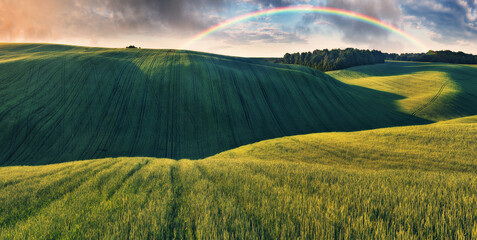Rainbow and dramatic gray sky with clouds landscape. picturesque hilly field
