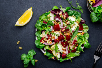 Beet and pear healthy salad with arugula, lamb lettuce, red onion, chard and walnut, black kitchen table. Fresh delicious vegan dish for healthy eating