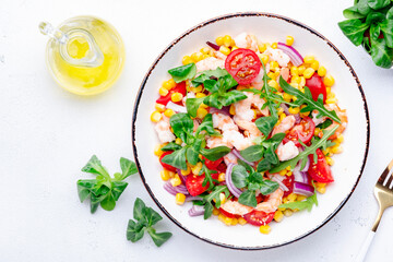 Delicious shrimp salad with sweet corn, cherry tomatoes, lamb lettuce and red onion on white table background. Top view
