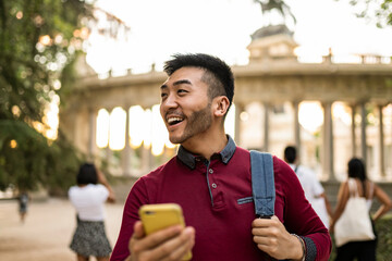 happy asian japanese tourist visiting european city at sunset, using smartphone to look at city map