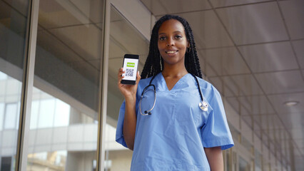 Low angle view of smiling African-American female surgeon show vaccination certificate at camera