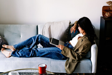Obraz premium Young asian women listening to music in headphones and dancing energetic and rhythm at couch. Attractive Asian girl looking at the smart phone sitting in the living room spending leisure time at home