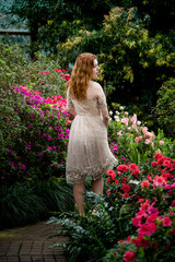 portrait of beautiful romantic redhead woman in pink dress walking with flowers in spring garden