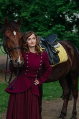 Foto op Canvas Beautiful elegant young woman in vintage dress stands next to cute horse on a walk in nature. Walk with a horse in the woods. Elegant aristocratic young lady holding horse by reins. Horses and people © Anastasiia