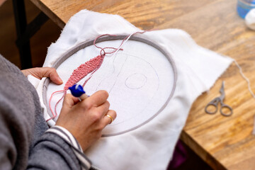 hands of an embroiderer embroidering balloons in the clouds with the punch needle technique