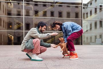 Fototapeta na wymiar male couple playing happy with their naughty little dog on the street, concept of family lifestyle with pets and love between people of the same sex, copy space for text