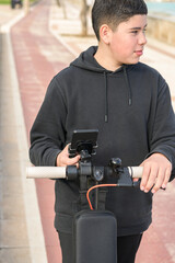 young teenager with a sideways glance riding an electric skateboard and using a smartphone application