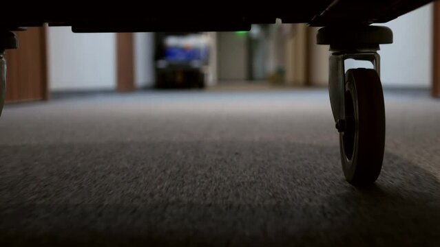 A close-up of the wheels of a guest luggage trolley in a hotel. The cart rolls down the hotel corridor at a low angle.
