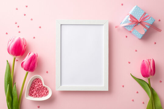 Mother's Day concept. Top view photo of photo frame pink tulips small blue present box with ribbon bow and heart shaped saucer with sprinkles on isolated pastel pink background with blank space