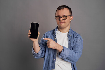Adult man with down syndrome showing empty screen of mobile phone on gray background