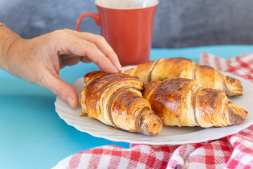 Hand of a girl holding a delicious chocolate filled croissant with a cup of coffee. High quality photo