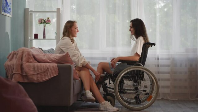 Supportive woman holds hands of girlfriend in wheelchair
