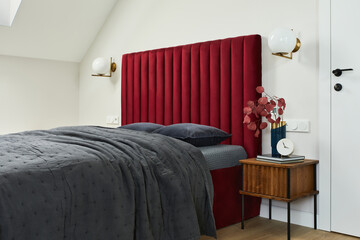 Minimalistic elegant bedroom interior with red bed, grey bedclothes and wooden furniture. Glamour...