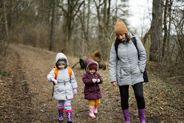 Mother and two daughters with backpacks walking along the forest road together.