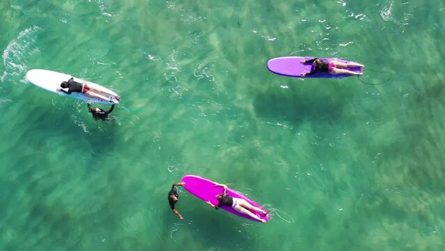 Aerial drone top down video of women surfers having surfing lesson in tropical exotic wavy bay with deep emerald sea