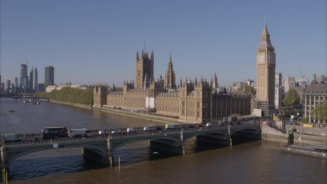 Aerial drone shot flying fast towards Westminster Bridge, Westminster Abbey and Big Ben over the River Thames with London Buses and traffic crossing Westminster Bridge on a bright clear sunny day.