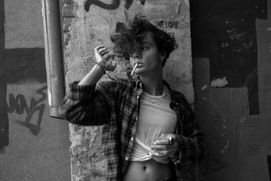 Black and white portrait of guy with cigarette leaning against old wall