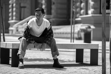 Stylish confident guy sitting on stone bench in city square