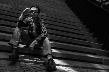 Confident guy sitting on stone stairs adjusting his glasses