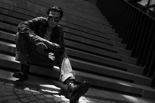 Relaxed Young Man Sitting On Steps Of Stone Stairs Outdoors