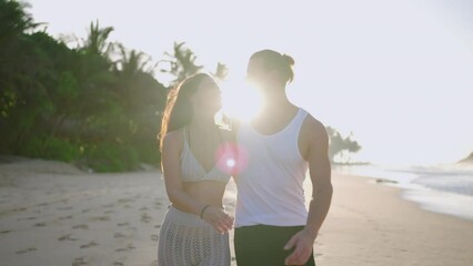 Young biracial happy couple hugging and walking on the beach together enjoying summer. Cheerful boyfriend and girlfriend relaxing and taking a walk at the seaside embracing at sunrise.